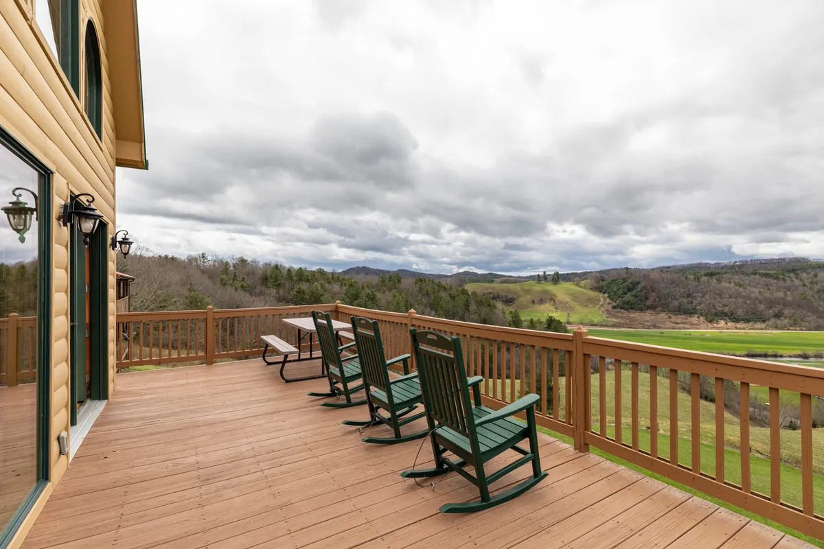 A peaceful exterior shot shows classic rocking chairs lined up along the deck railing, overlooking a vast mountain vista. The sky hints at changing weather, with the promise of stargazing at night or watching storms roll in.