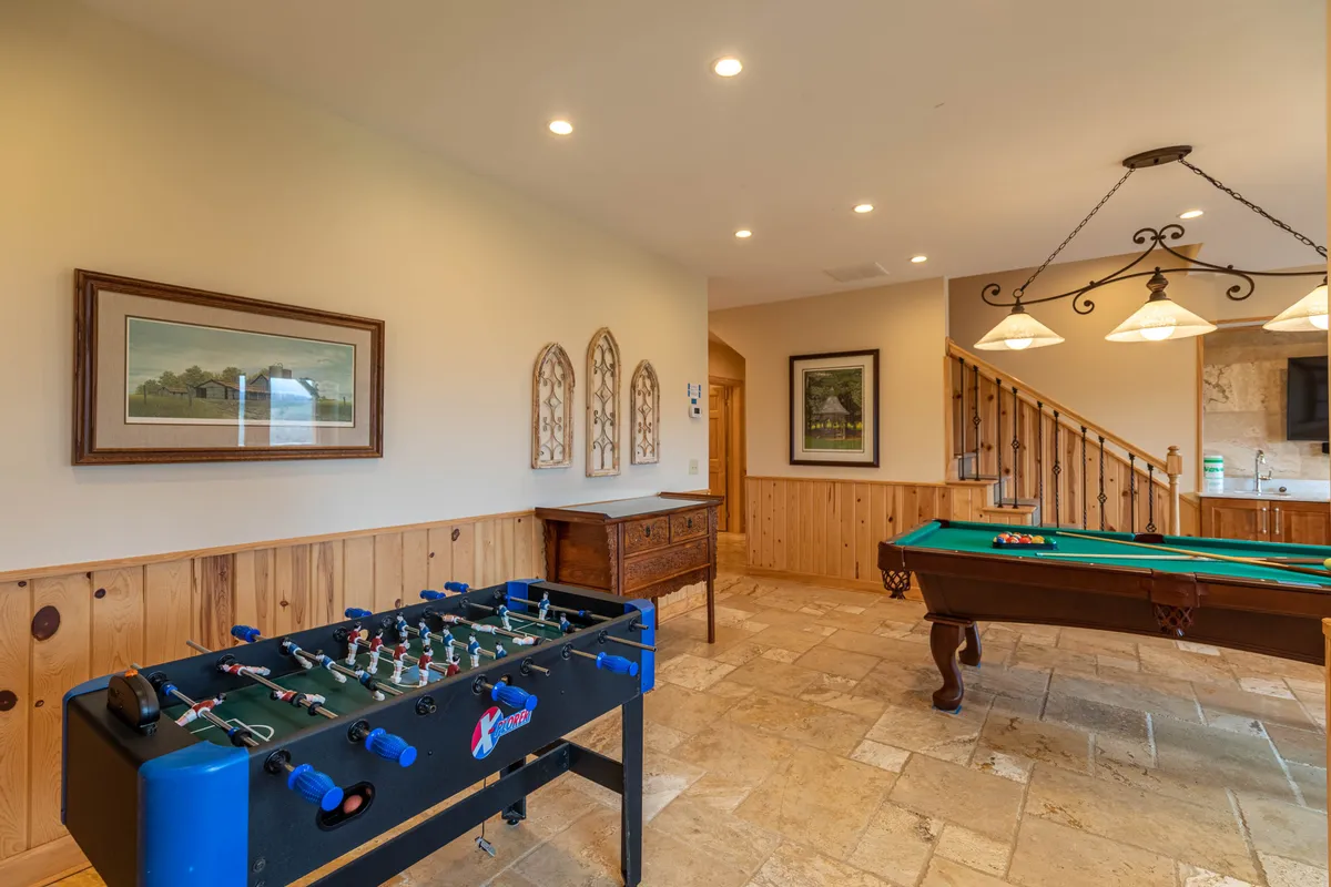 A playful interior showcasing both a foosball table and a pool table side by side, with tasteful framed artwork and a wooden cabinet completing the scene. The setup invites guests to enjoy lively rounds of games in a cozy, relaxed setting.