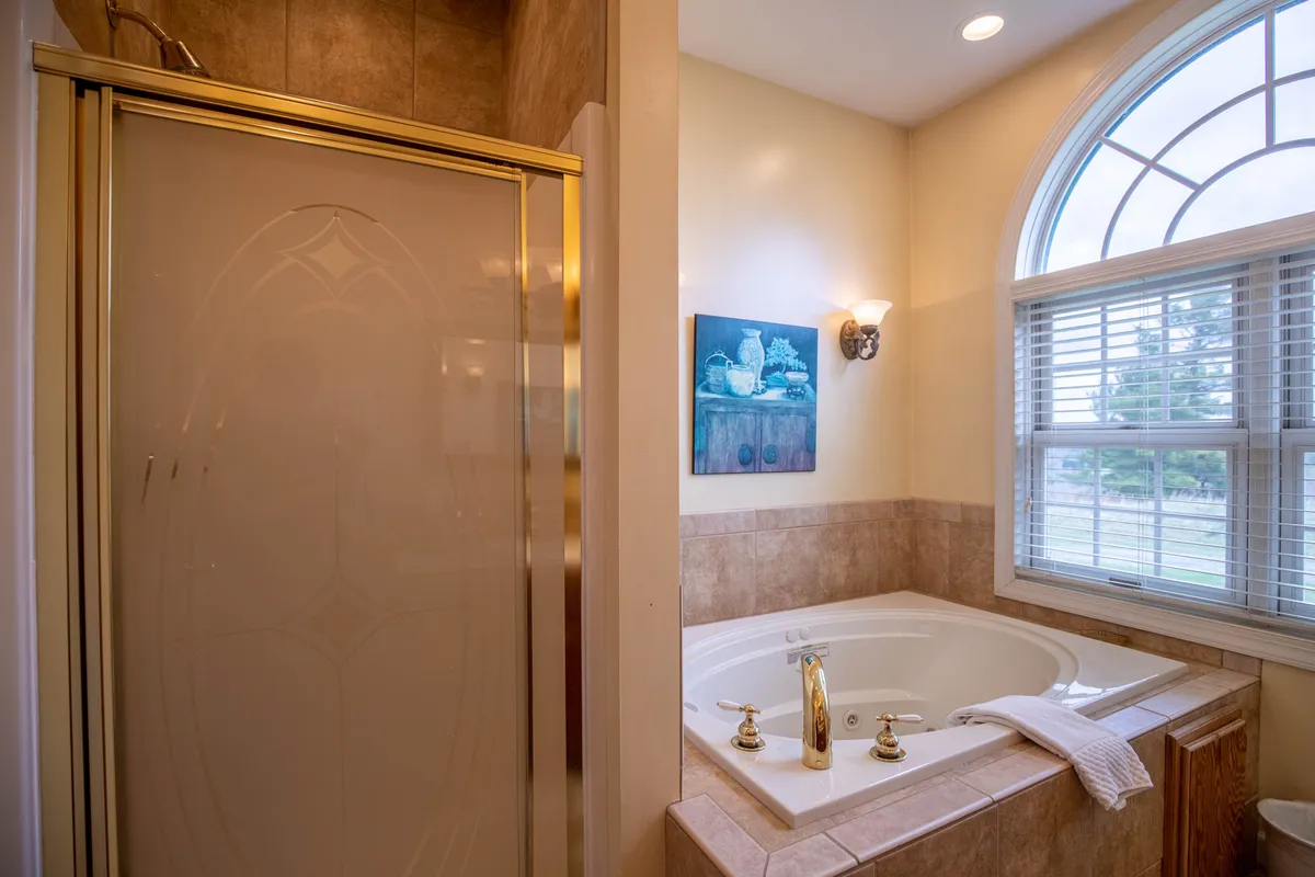 A luxurious bathroom featuring a jacuzzi whirlpool tub, a separate shower enclosure with glass doors, decorative wall art, and a window that invites in natural light, creating a spa-like ambiance.