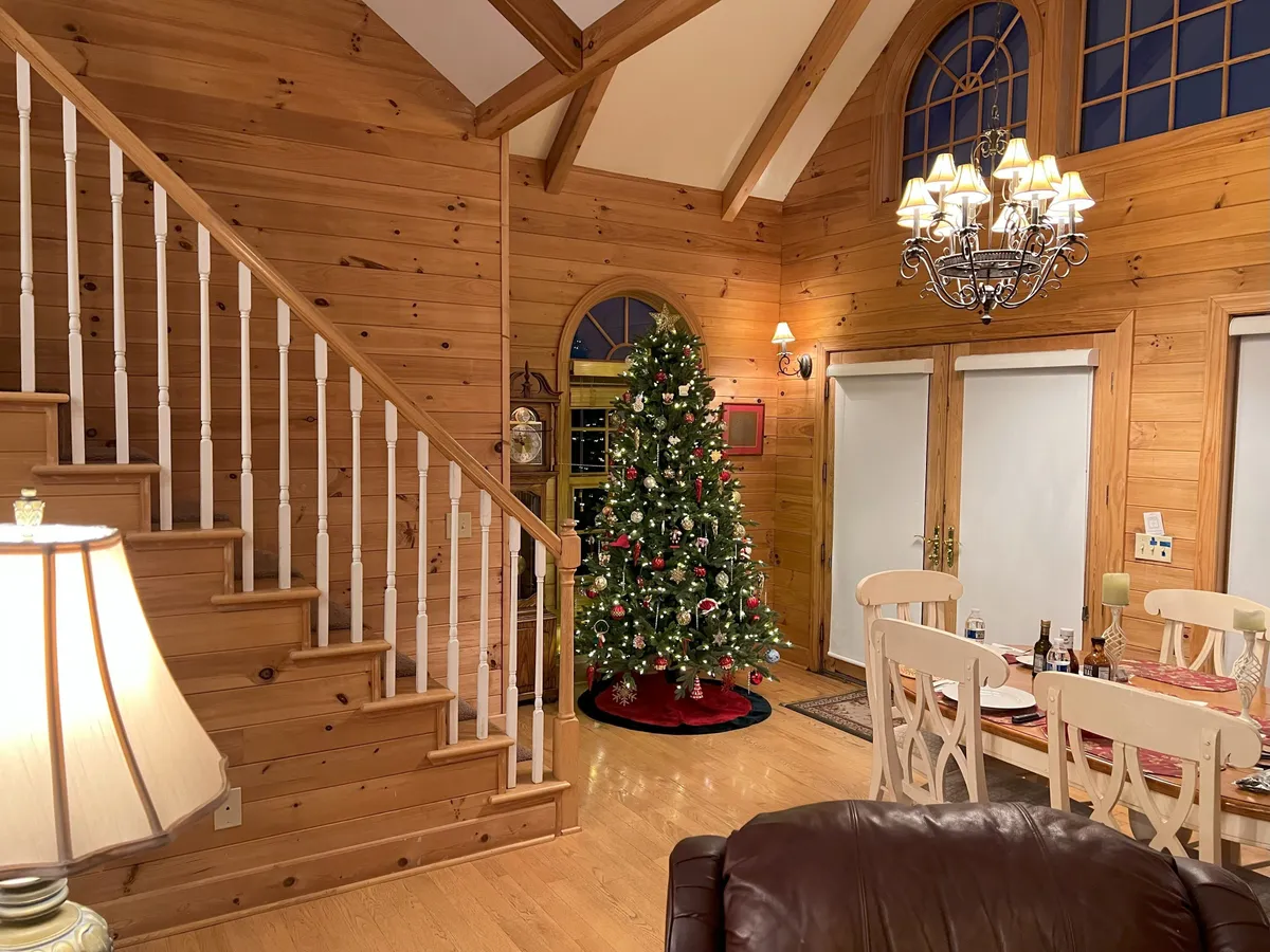 A warm, inviting dining area with a large table, chandelier, and Christmas tree, suggesting festive gatherings. The setup is perfect for family dinners and group celebrations, with the dining table positioned to enjoy wraparound views through the windows.