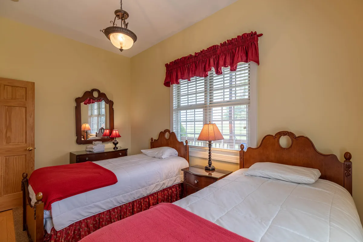 A cheerful twin bedroom with two cozy beds adorned with red bed skirts, soft lighting from bedside lamps, and a mirror that adds a sense of space. The room feels playful yet restful, perfect for children or friends sharing a room.