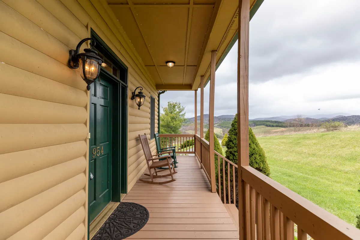 A welcoming porch with rocking chairs facing out toward mountains and a well-kept lawn, offering a relaxed vantage point for enjoying scenic views. Lanterns and the front door suggest a seamless transition from indoors to the outdoors, reinforcing the sense of easy access to natural beauty and nearby adventures.
