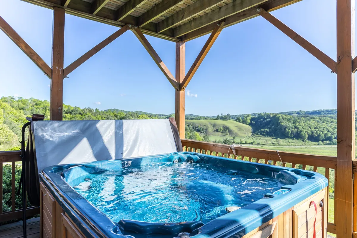 An inviting deck featuring a wooden hot tub, surrounded by sweeping mountain views under an open sky. The wooden structure suggests a perfect spot for outdoor relaxation, and there's ample space for socializing or enjoying a meal outside.