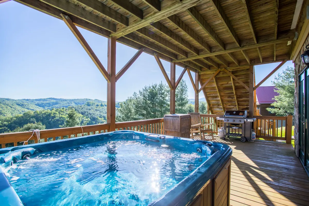 An inviting exterior scene with the hot tub in the foreground and an expansive mountain view beyond. The wooden deck also features an outdoor grill, signaling possibilities for social meals and gatherings in the fresh air.