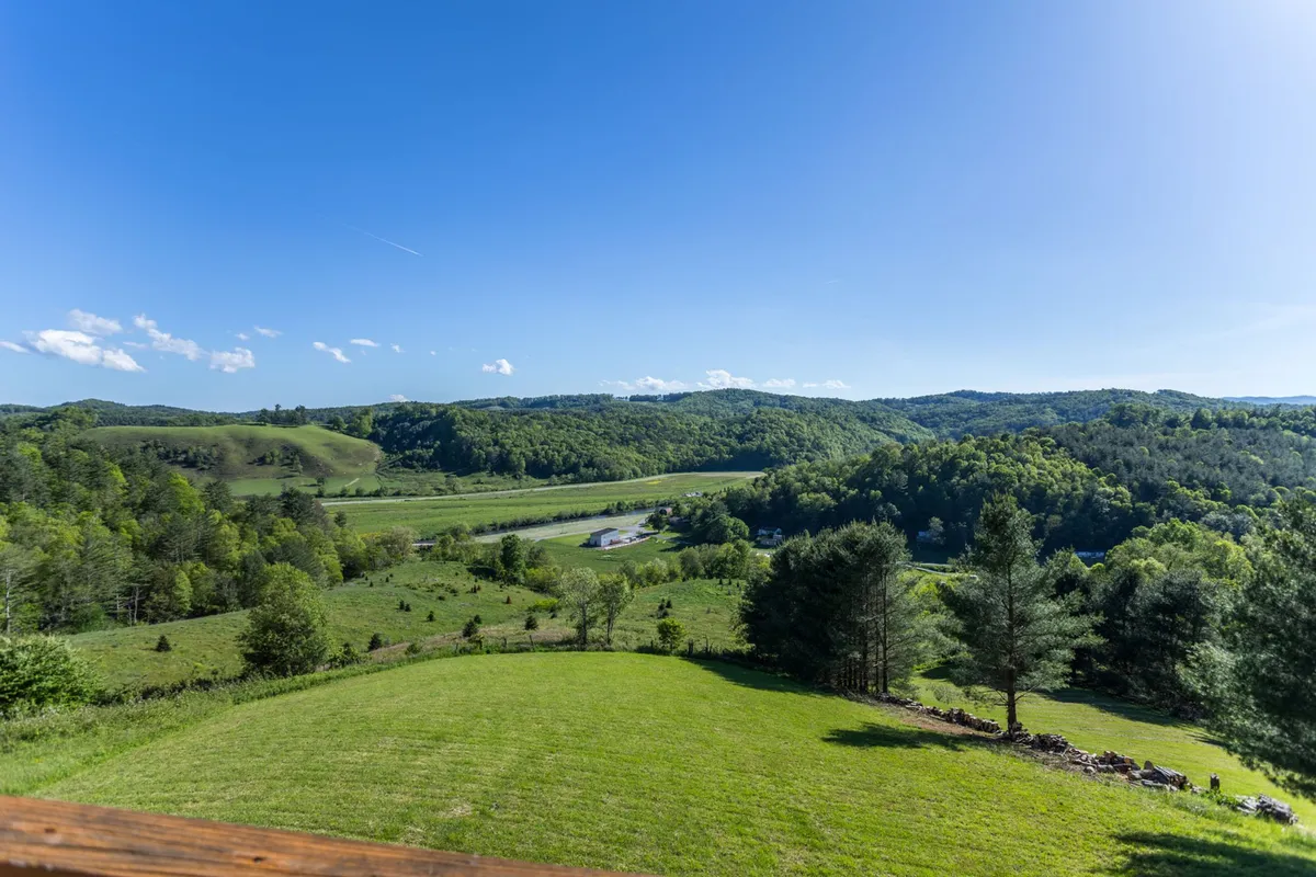 A broad, panoramic view featuring rolling green hills, lush vegetation, and a meandering river under a clear blue sky. The river is the focal point, winding gracefully through the landscape and inviting thoughts of kayaking, fishing, or tubing. The scene radiates calm and the untouched beauty of the outdoors, with plenty of visual cues suggesting opportunities for adventure and exploration.