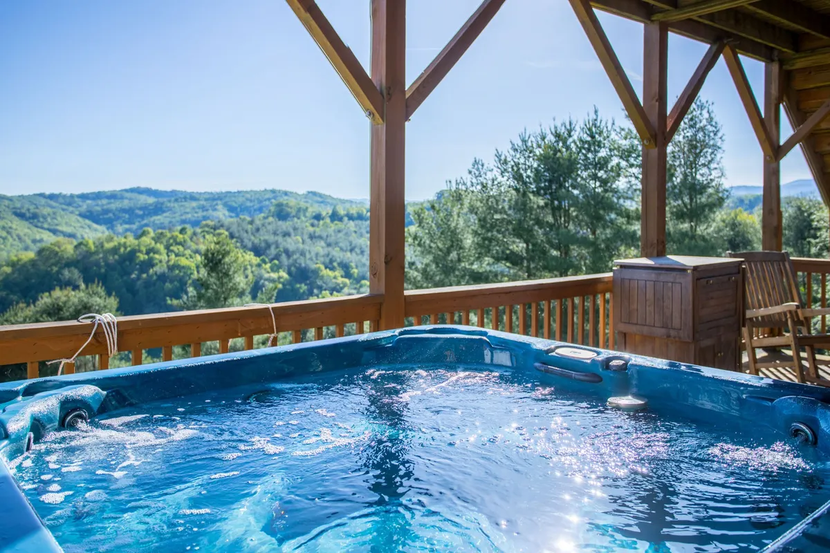 This image captures a tranquil scene on the wooden deck, featuring a private hot tub positioned to maximize breathtaking views of the surrounding mountains. The setting sun casts a warm glow over the landscape, enhancing the inviting atmosphere for relaxation and outdoor enjoyment.