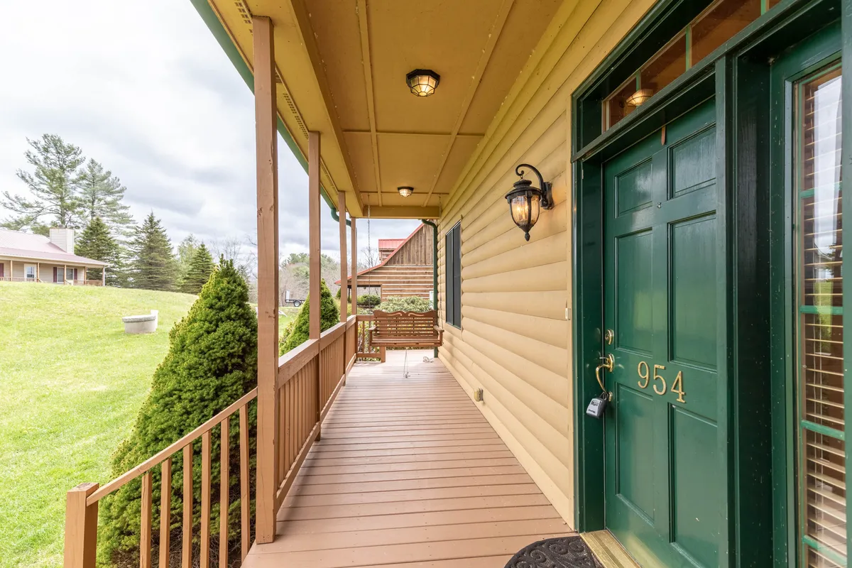 This image captures the inviting front porch of the cabin, featuring a green front door, lantern light fixtures, a wooden porch swing, and a well-manicured lawn. The porch swing and welcoming entrance hint at relaxed moments and the family-friendly atmosphere that awaits inside.