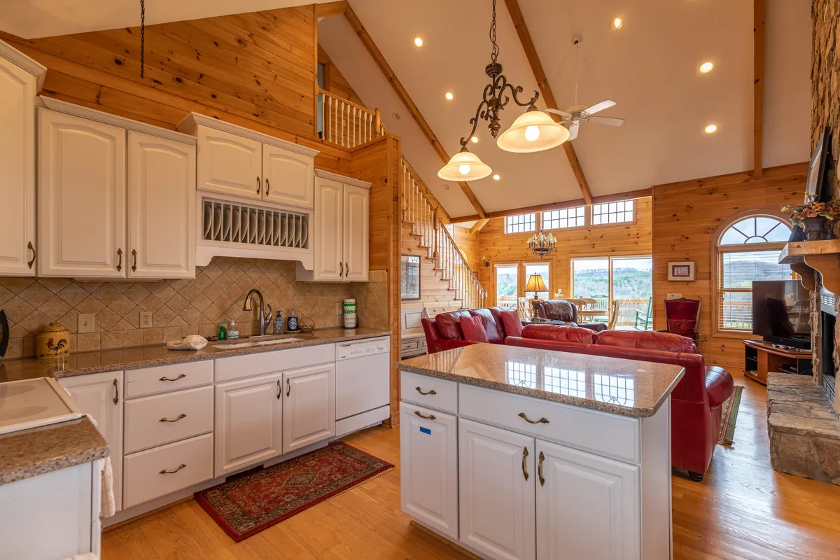 An open-concept kitchen and living area featuring a kitchen island, red leather sofas, and large windows offering panoramic views. The space is designed for both cooking and entertaining, with seamless transitions between the kitchen and living zones.